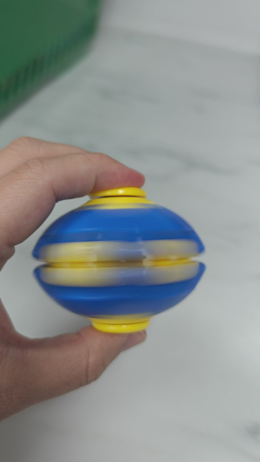 Vertical demonstration of the blue and yellow press-to-spin fidget ball